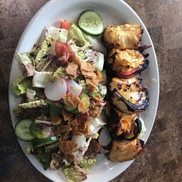 Grilled chicken skewers with a side of fresh Mediterranean salad topped with pita chips.