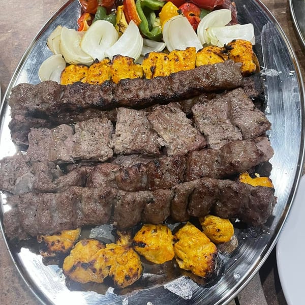 A large platter of grilled Mediterranean koobideh and chicken kebabs with onions and bell peppers.