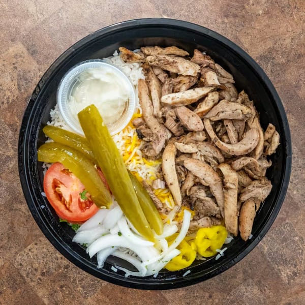 Overhead view of a Mediterranean chicken and rice bowl with pickles, tomatoes, onions, and sauce.