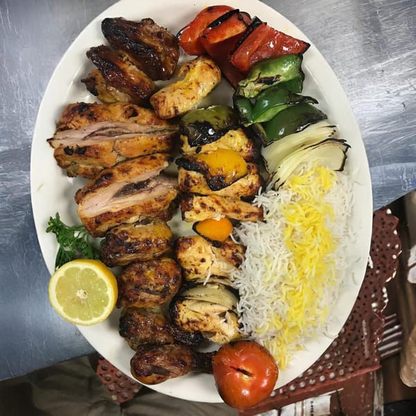 A large platter of grilled Mediterranean chicken, vegetables, and rice with a lemon half.